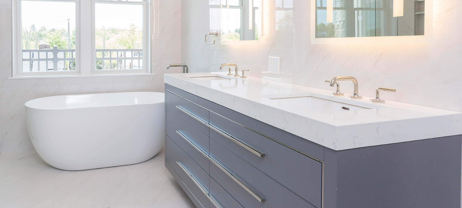 White bathtub, vanity with silver fixtures, lighted mirrors