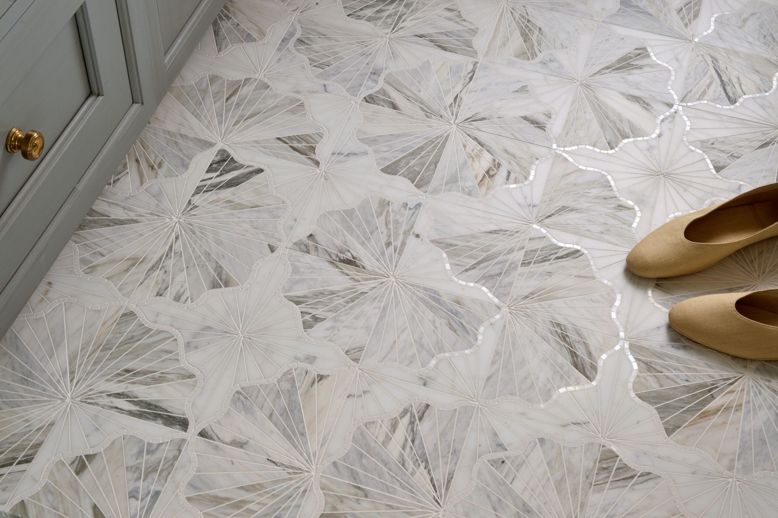 white marble tiles with a pattern, tan shoes, grey cabinet with gold knobs