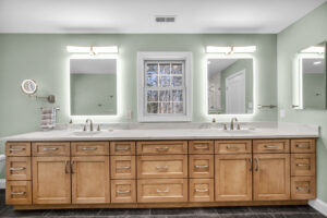 large wood vanity with white counter tops and illuminated mirros